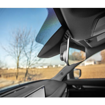 A car-mounted rearview mirror with an integrated camera lens, shown installed on a vehicle's sun visor. The image is taken from inside the car cabin, with a blurred outdoor landscape visible through the windshield.
Tracer Mensa FHD Videoregistrator 4.0D, Rezhim na parkirane