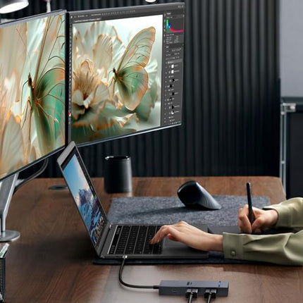 Person using a laptop with two monitors displaying butterfly images on a desk.