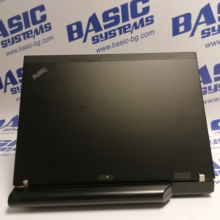 Поглед от задна страна на Лаптоп втора употреба Lenovo ThinkPad X201 - CPU i5-580М, 4GB RAM, 128GB SSD. На бял фон с лого basic systems и www.basic-bg.com. Виждат логото Lenovo ThinkPad на черен корпус на дисплея и батерията.